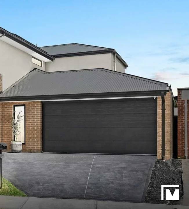Modern house in Eltham with a black double garage door, brick walls, concrete driveway, and a small potted plant by the entrance.