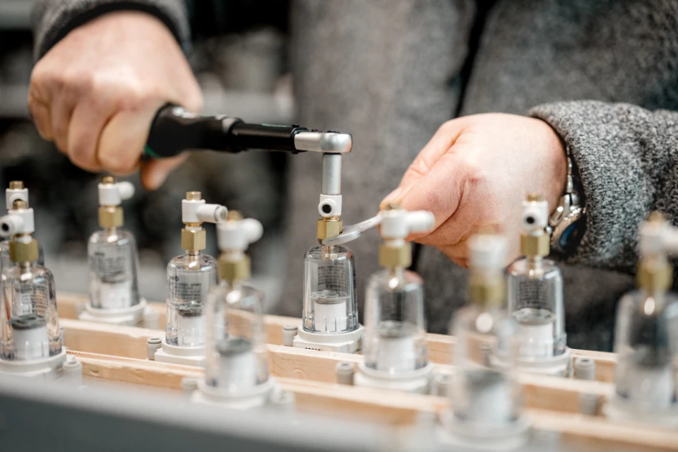 Person montiert präzise mechanische Bauteile an einer Produktionslinie mit Werkzeugen.