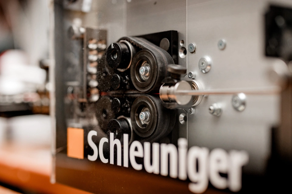 Nahaufnahme einer Schleuniger-Maschine, die Kabel oder Drähte bearbeitet, mit sichtbaren Rollen und Metallteilen.