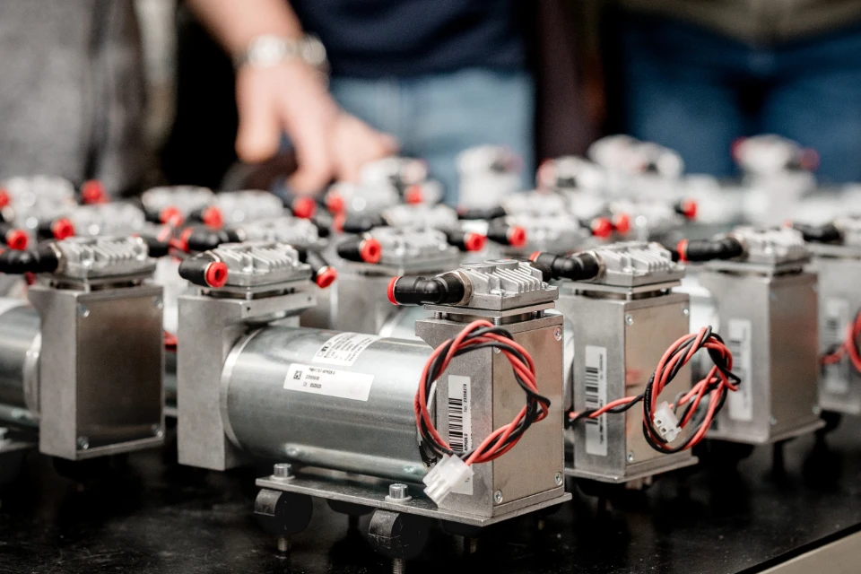 Mehrere identische medizinische Geräteprototypen mit Metallgehäuse, schwarzen und roten Kabeln auf einem Arbeitstisch.