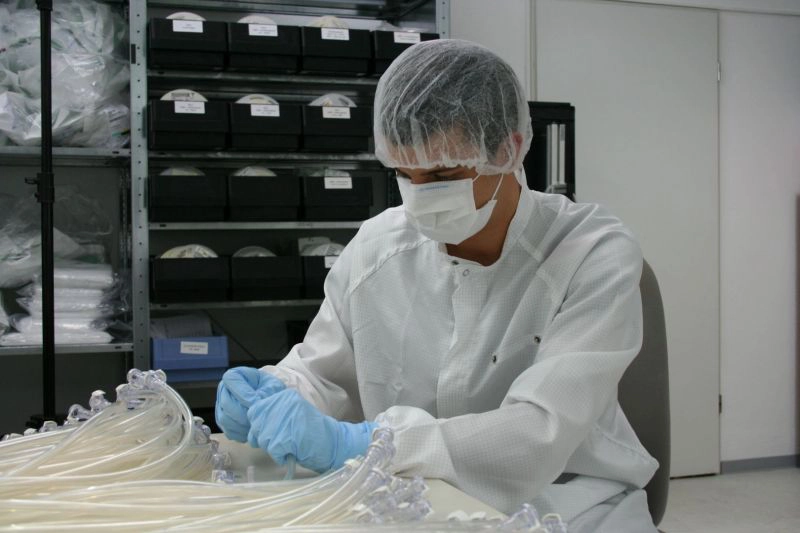 Mitarbeiter in Schutzkleidung, Maske und Haarnetz montiert oder überprüft medizinische Schläuche in einer sauberen Produktionsumgebung.