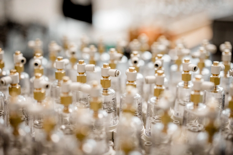 Viele kleine, transparente Kunststoffbehälter mit goldfarbenen und weißen Anschlussstücken, unscharf im Hintergrund.