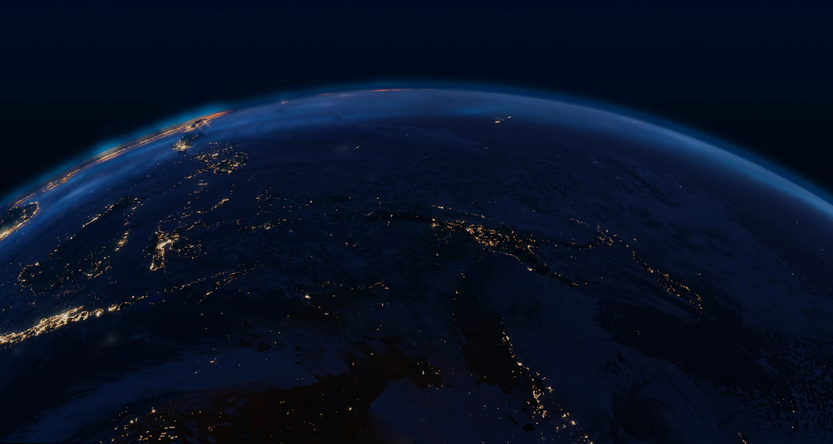 View of Earth at night from space showing illuminated city lights along coastal regions under a dark sky.