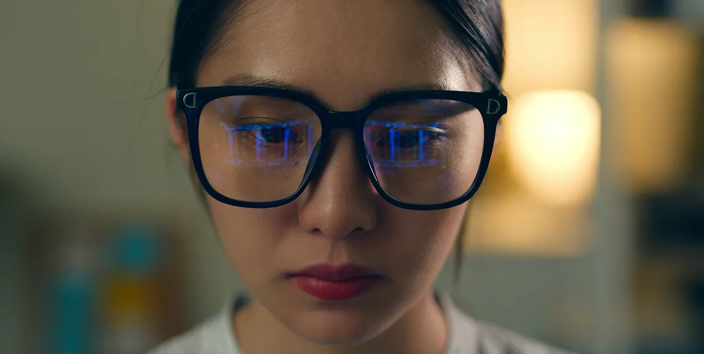 Close-up of a person wearing large black-rimmed glasses with blue light reflections on the lenses.
