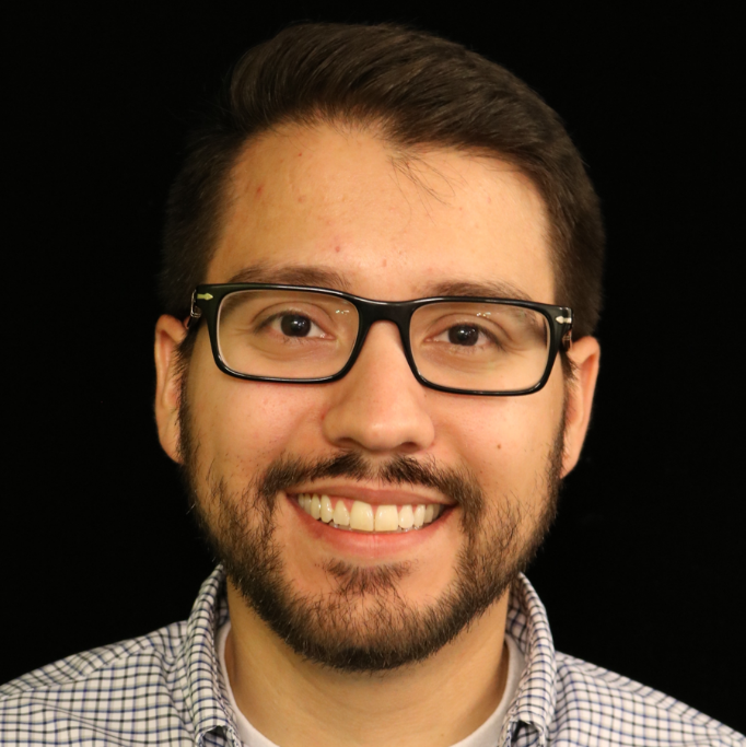 Smiling man with glasses, beard, and checkered shirt on black background.