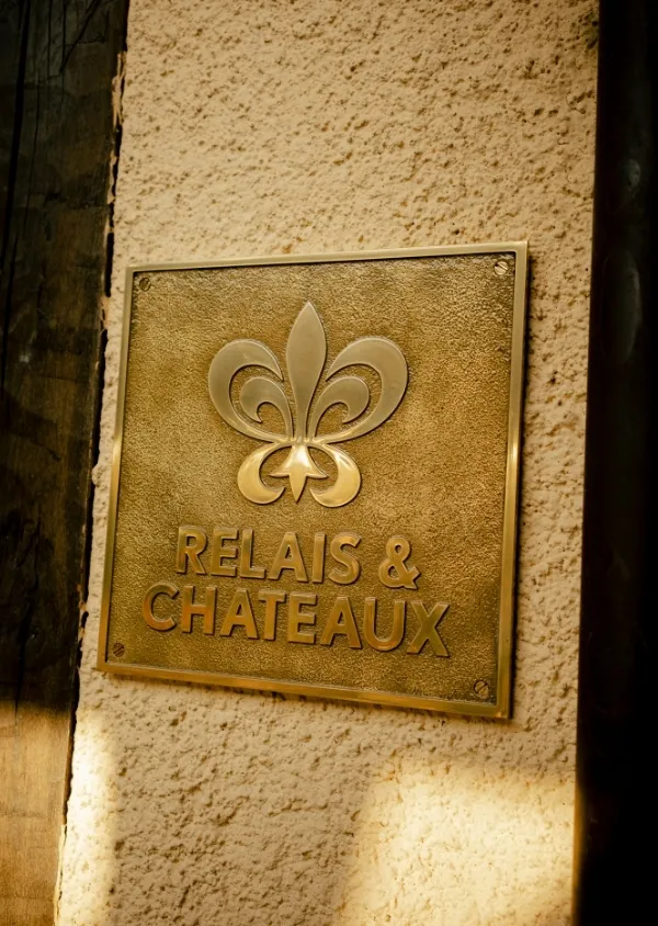 Gold plate with a stylized lily and the text 'RELAIS & CHATEAUX' fixed on a beige plaster wall.