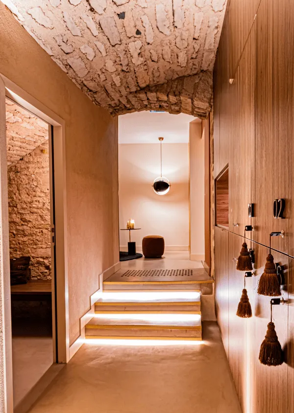 Corridoio moderno con pareti in pietra, scala illuminata, mobili in legno chiaro e sospensione sferica.