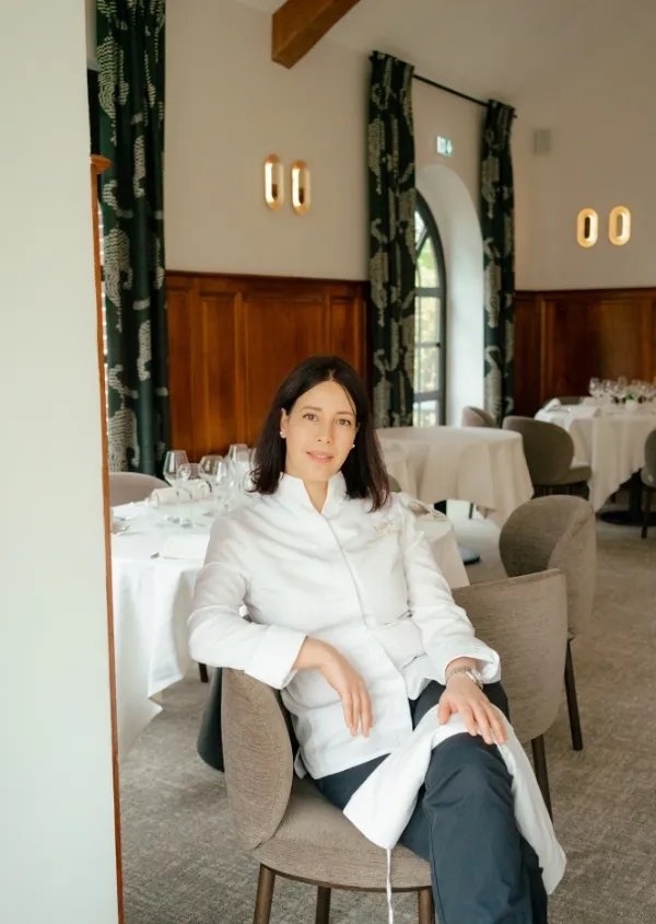 Lo chef Nawal Rezagui seduto su una sedia in un elegante ristorante con tavoli apparecchiati.
