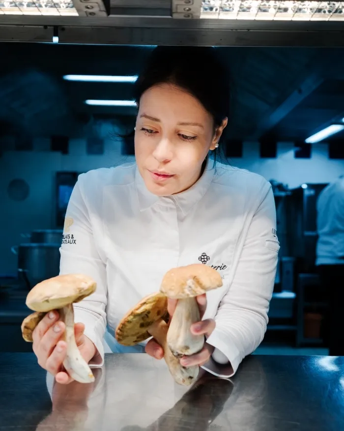 Uno chef in giacca bianca con in mano diversi funghi di legno in una cucina professionale.