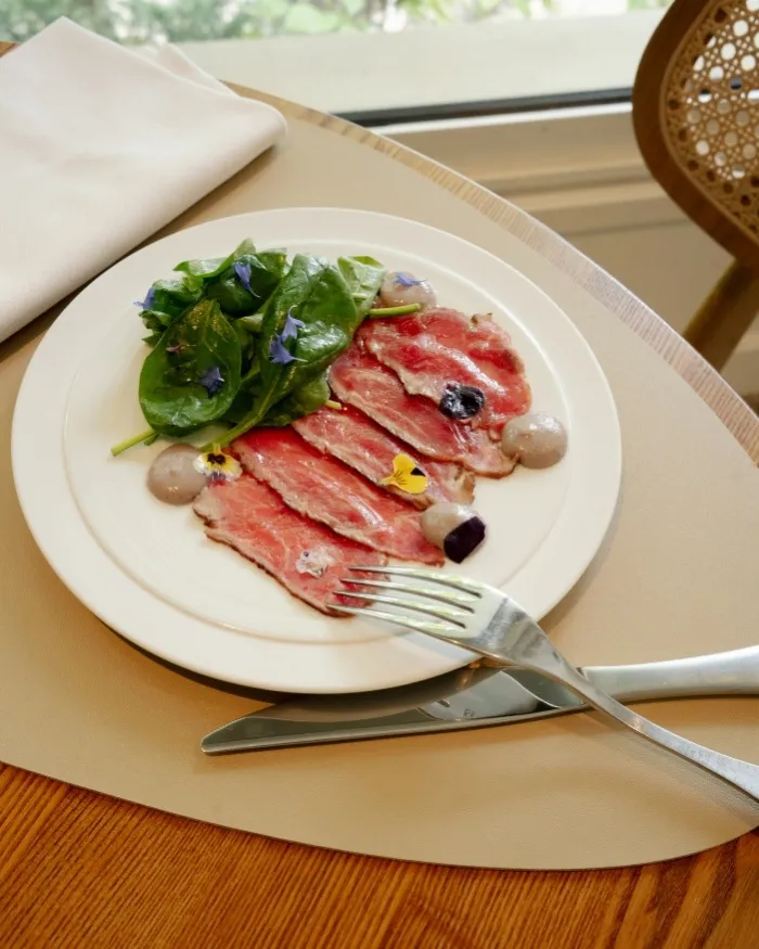 Piatto di carpaccio di manzo decorato con fiori commestibili e servito con insalata di giovani germogli verdi.