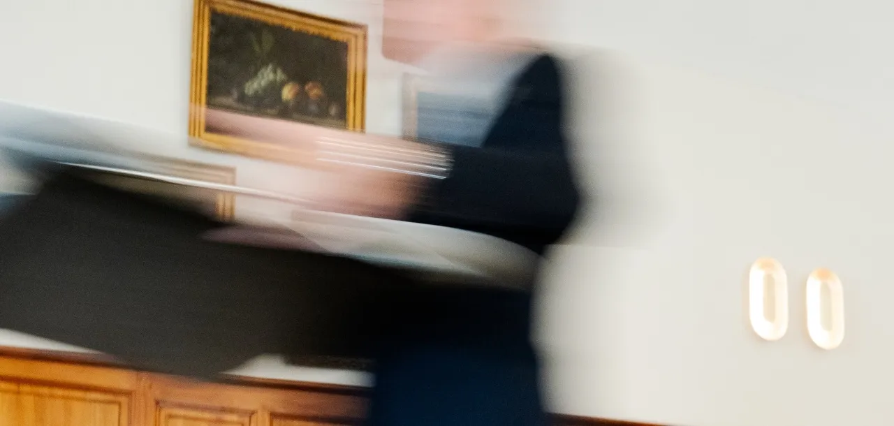 Persona in rapido movimento che trasporta una valigetta in un ufficio con quadri incorniciati sul muro.