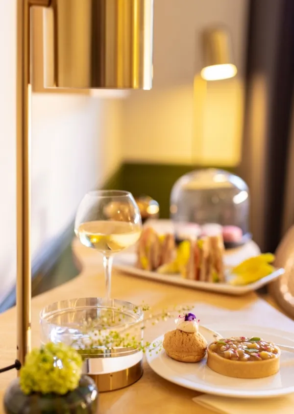 Bicchiere di vino bianco, cupcake e panini su un tavolo con una lampada moderna e decorazioni floreali.