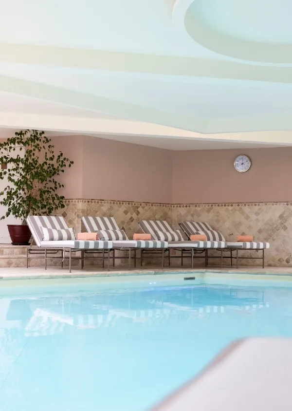 Piscine intérieure avec plusieurs chaises longues rayées avec serviettes orange et plante en pot dans un coin.