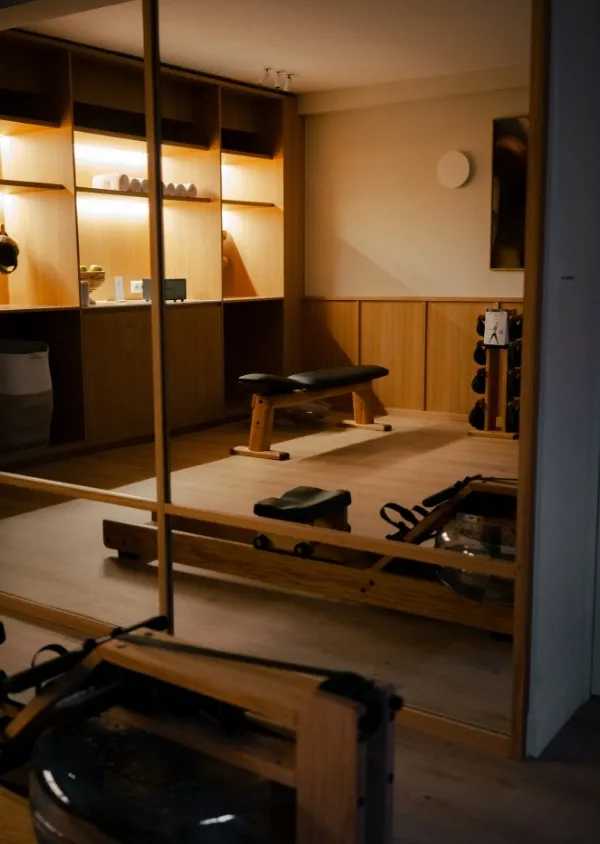 Salle de sport intérieure avec un banc d'exercice en bois et un rack de poids, éclairée chaleureusement.
