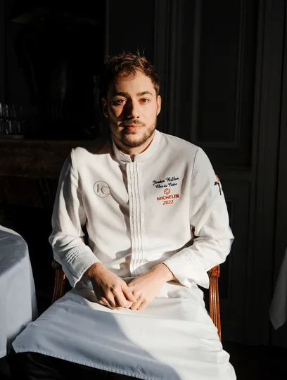 Junger Koch sitzt und trägt eine weiße Jacke, die von Michelin 2022 bestickt wurde.