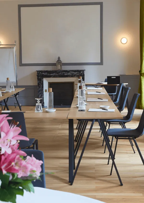 Meeting room with U-shaped wooden tables, black chairs, water bottles, and pink flowers in the foreground.