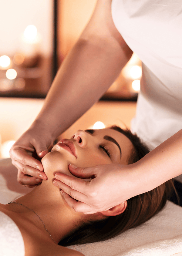 A woman receives a relaxing facial massage in a soothing spa environment with dimmed lights.