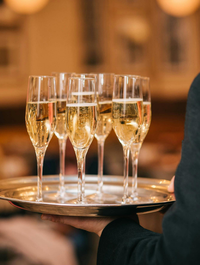 Eine Person, die ein Tablett mit mehreren gefüllten Champagnerflöten in der Hand hält.