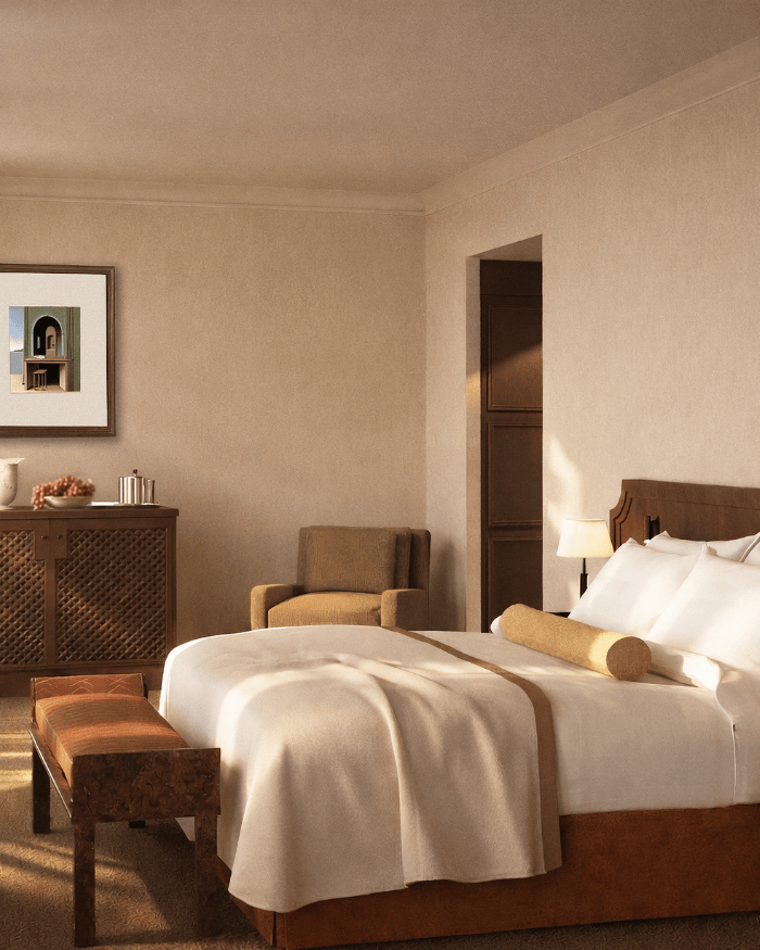 An inviting close-up of the king bed in the Classic Suite, highlighting the soft linen bed linen, textured bench, and carved wooden dresser under a contemporary portrait.