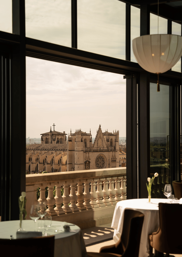 View of a historic cathedral seen from a restaurant balcony with tables and chairs in the foreground.