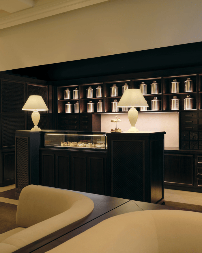 Elegant tea shop counter with glass display of pastries, illuminated lamps, and shelves of canisters.