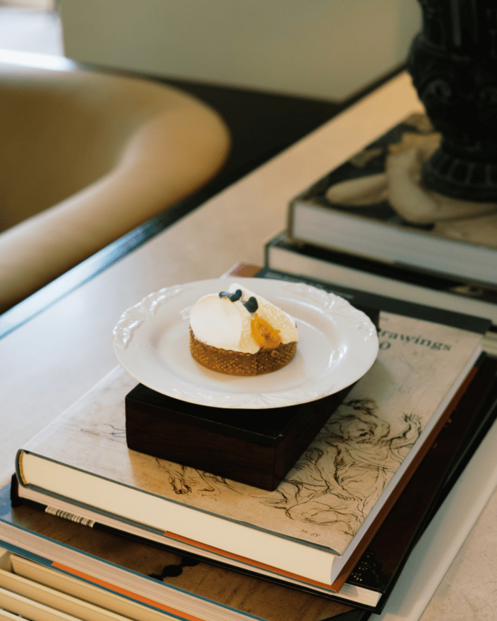 Small dessert with white cream, blueberries, and an orange garnish on a plate atop stacked books.