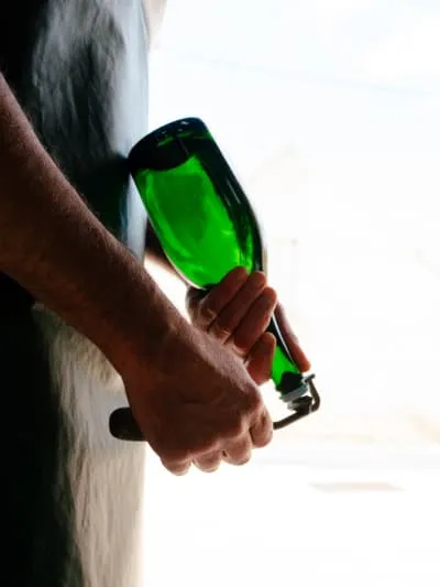Opening a green champagne bottle with a corkscrew.