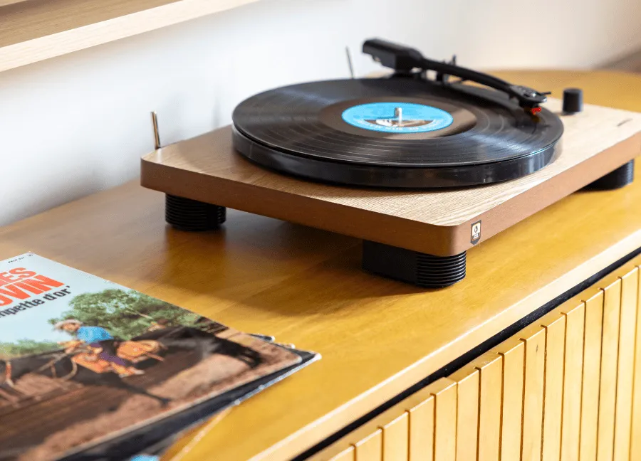 Giradischi in legno chiaro con un disco in riproduzione, posato su un mobile in legno accanto alle copertine degli album.