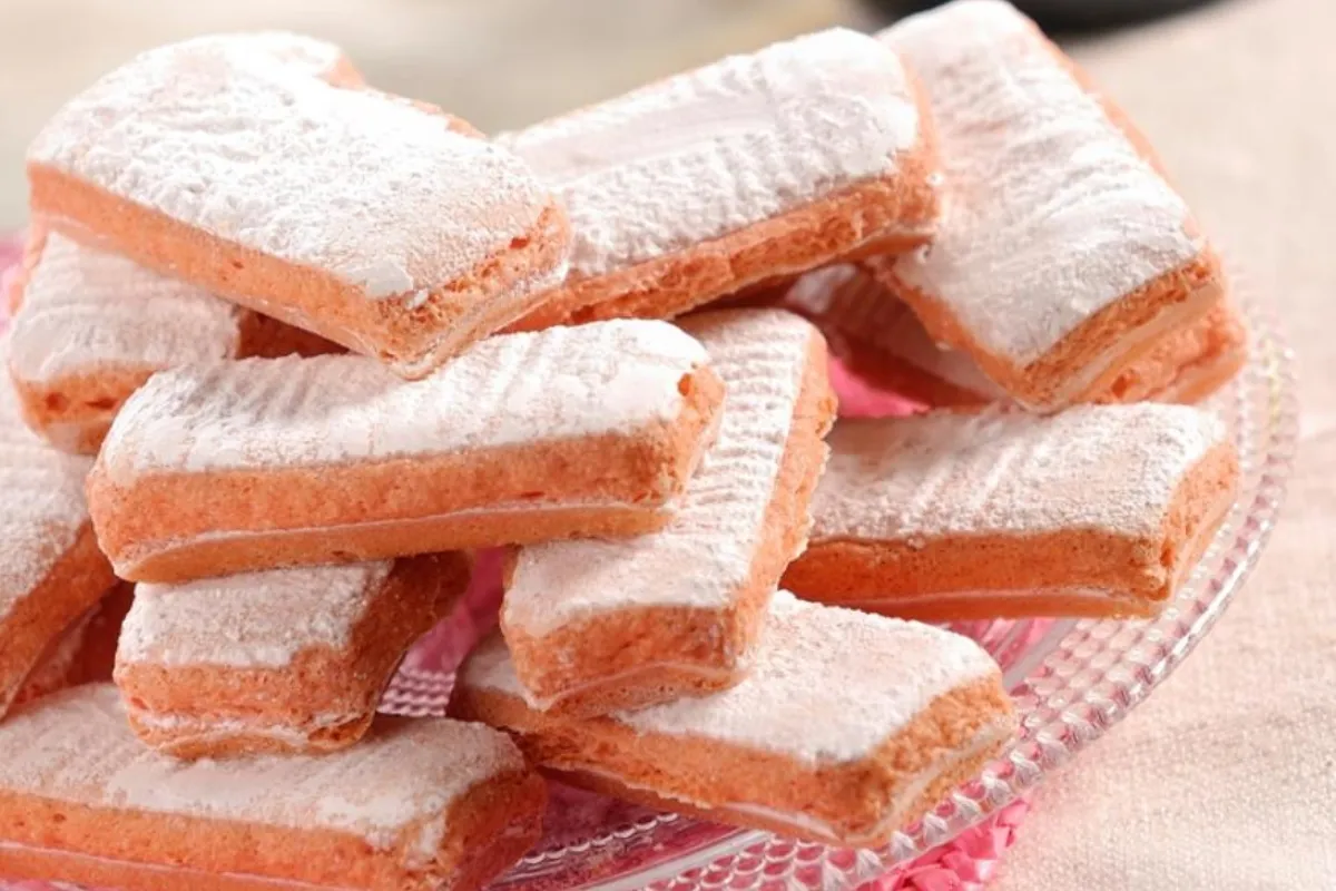 Pile of pink cookies sprinkled with icing sugar on a platter.