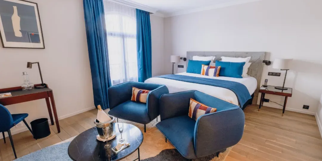 Guigone Junior Suite mit Doppelbett und Wohnbereich mit blauen Sesseln in der Hostellerie Cèdre & Spa in Beaune.