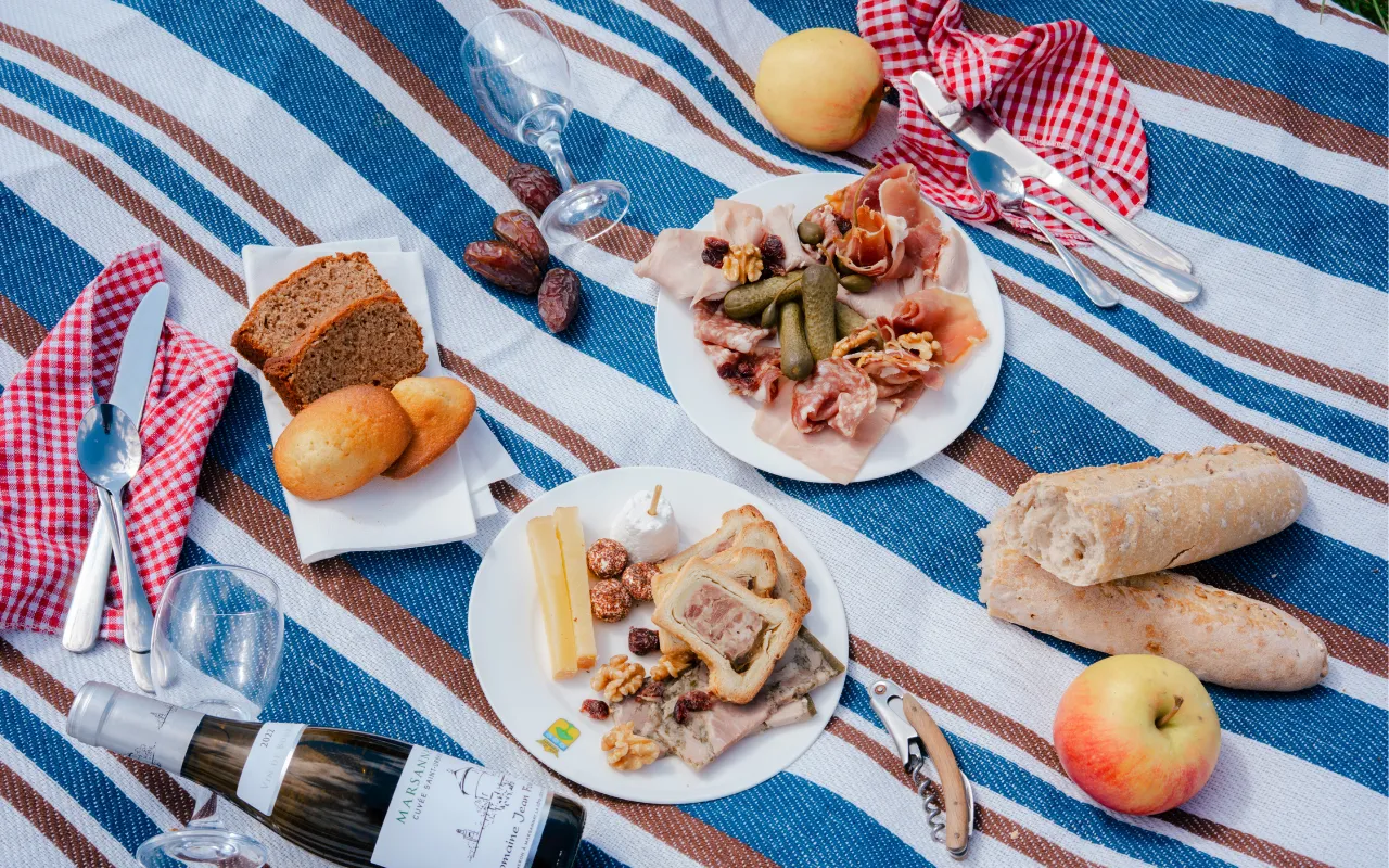 Burgundy picnic with charcuterie, cheeses, bread and a bottle of wine on a striped tablecloth.
