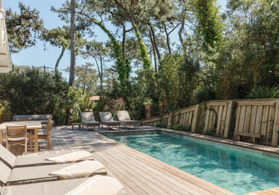 Piscina riscaldata e terrazza in legno della casa Oyat a Cap Ferret circondata da pini.