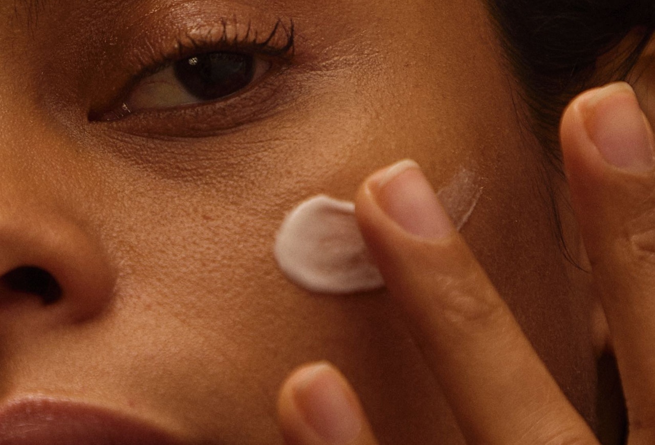 Close-up of a woman's face applying a skincare cream with her fingertips to her cheek, near her eye. Spa Apoticari, Villa Florentine Lyon
