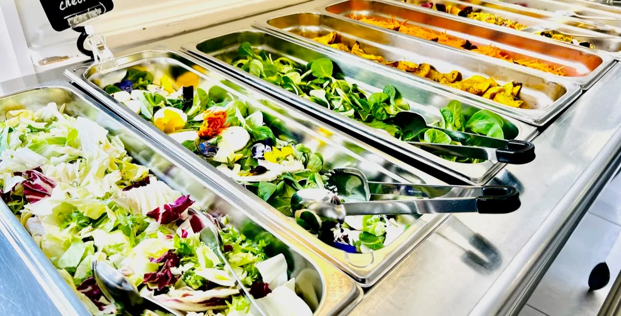 Buffet salad bar with trays of fresh leafy greens, mixed greens with edible flowers, and other salad ingredients.