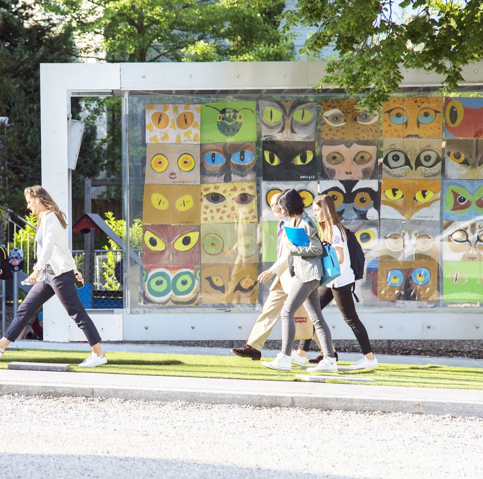 Four people walking on a sidewalk in front of a glass display featuring colorful paintings of various stylized eyes.
