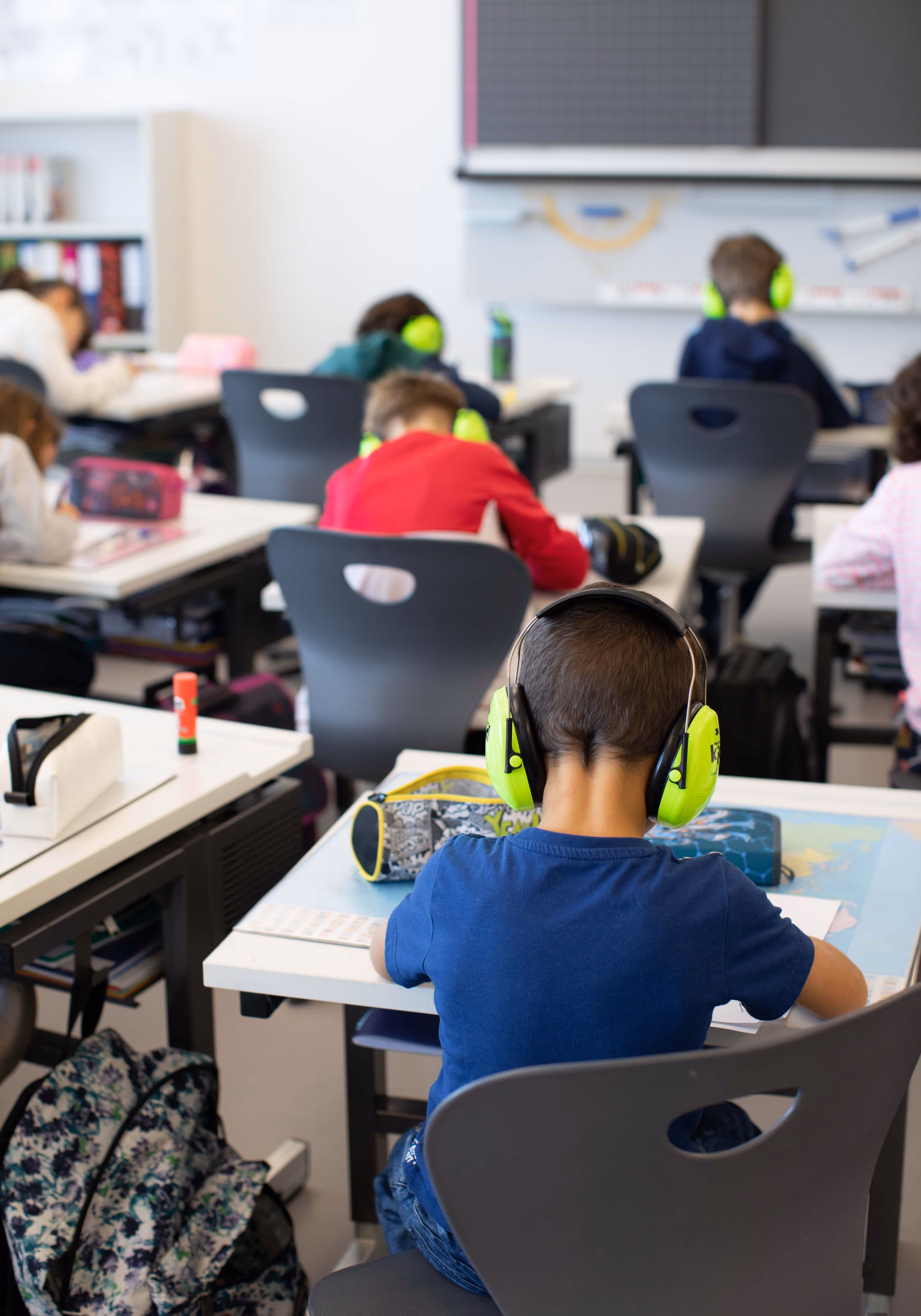 Primary school students sitting at desks wearing bright green headphones and focused on their work in a classroom.