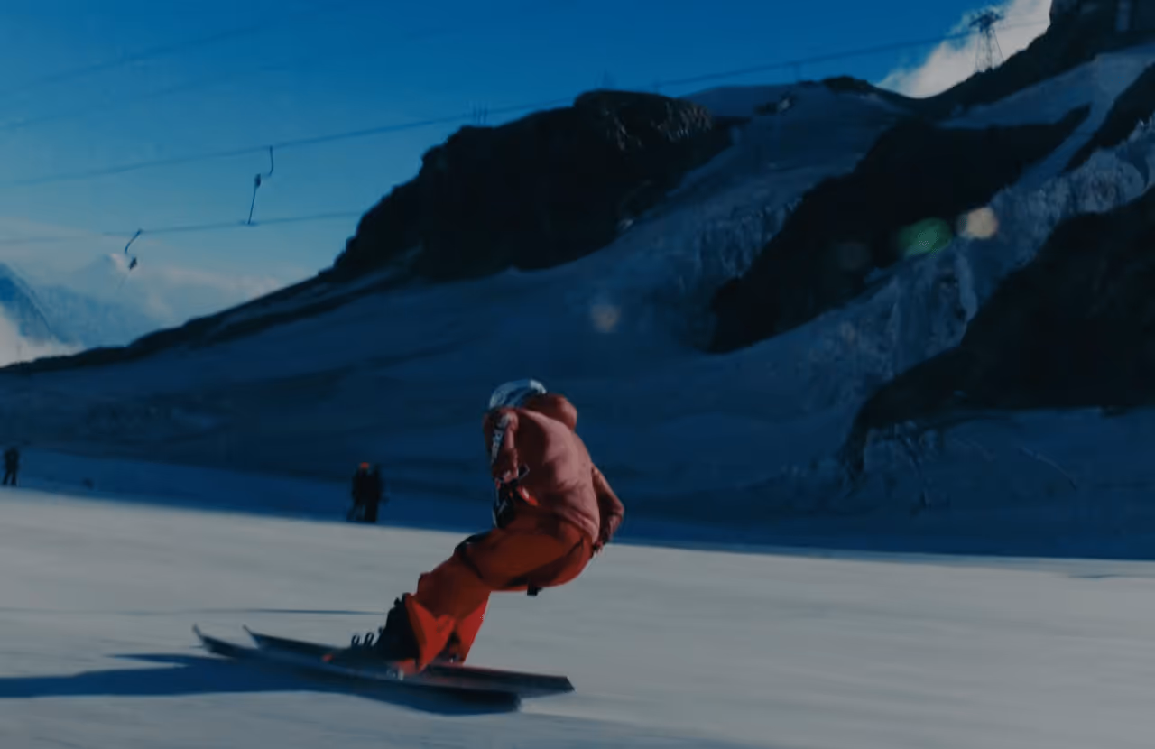 Snowboarder in red outfit carving down a snowy mountain slope with dark rocky peaks in the background.