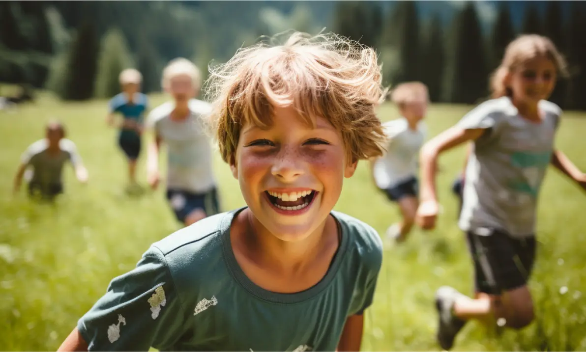 Smiling boy with tousled hair running outdoors on green grass with other children in the background.