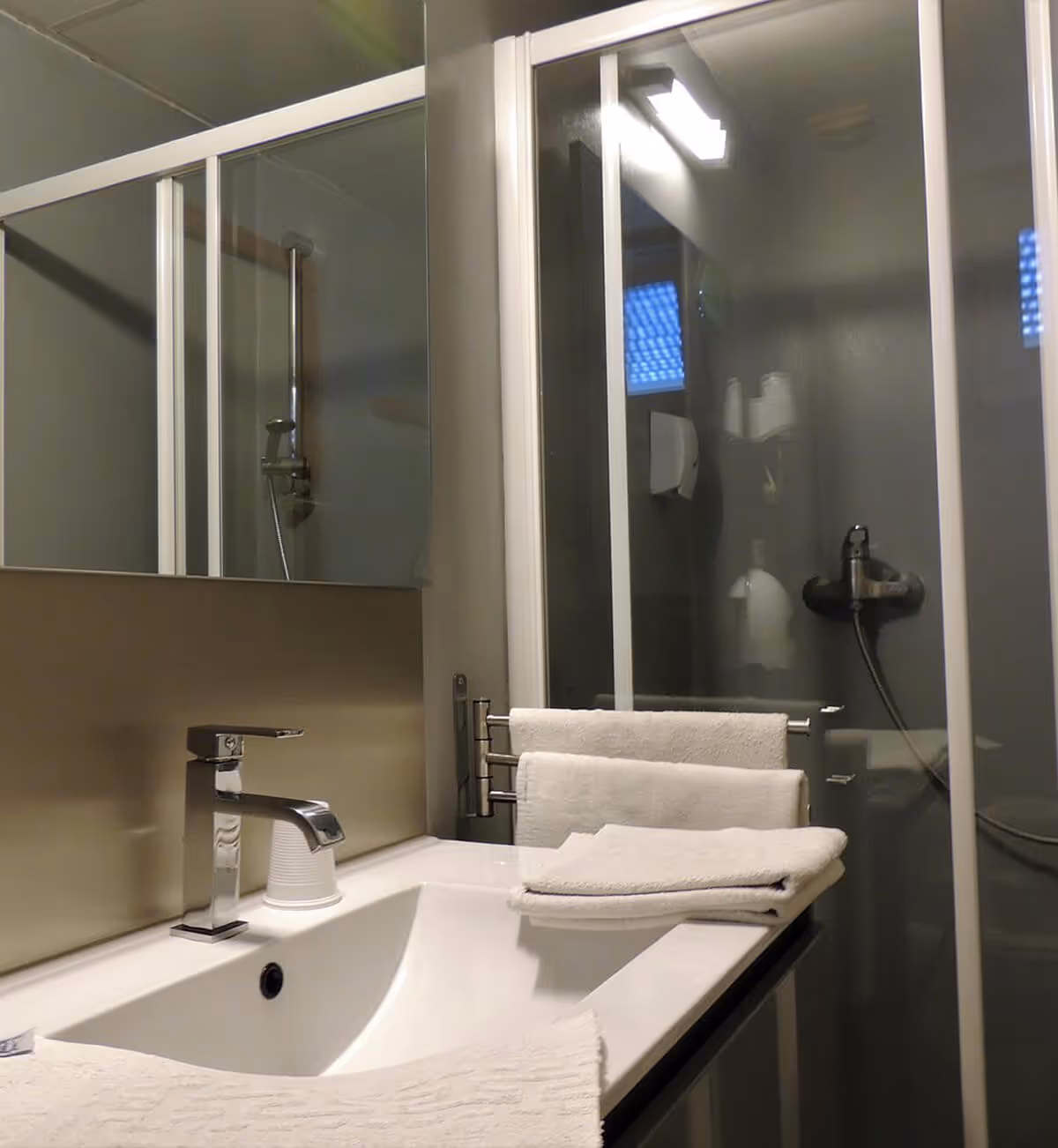 Salle de bains moderne avec lavabo blanc, robinet chromé, serviettes pliées et douche vitrée.