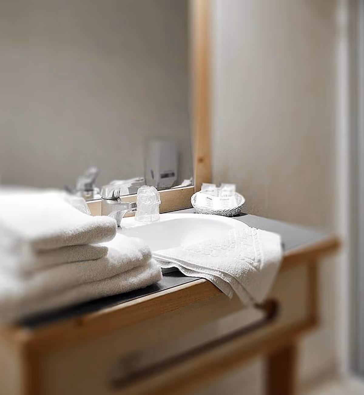 Lavabo de salle de bain avec serviettes blanches pliées, robinet, verre et panier contenant des articles de toilette sur le comptoir.