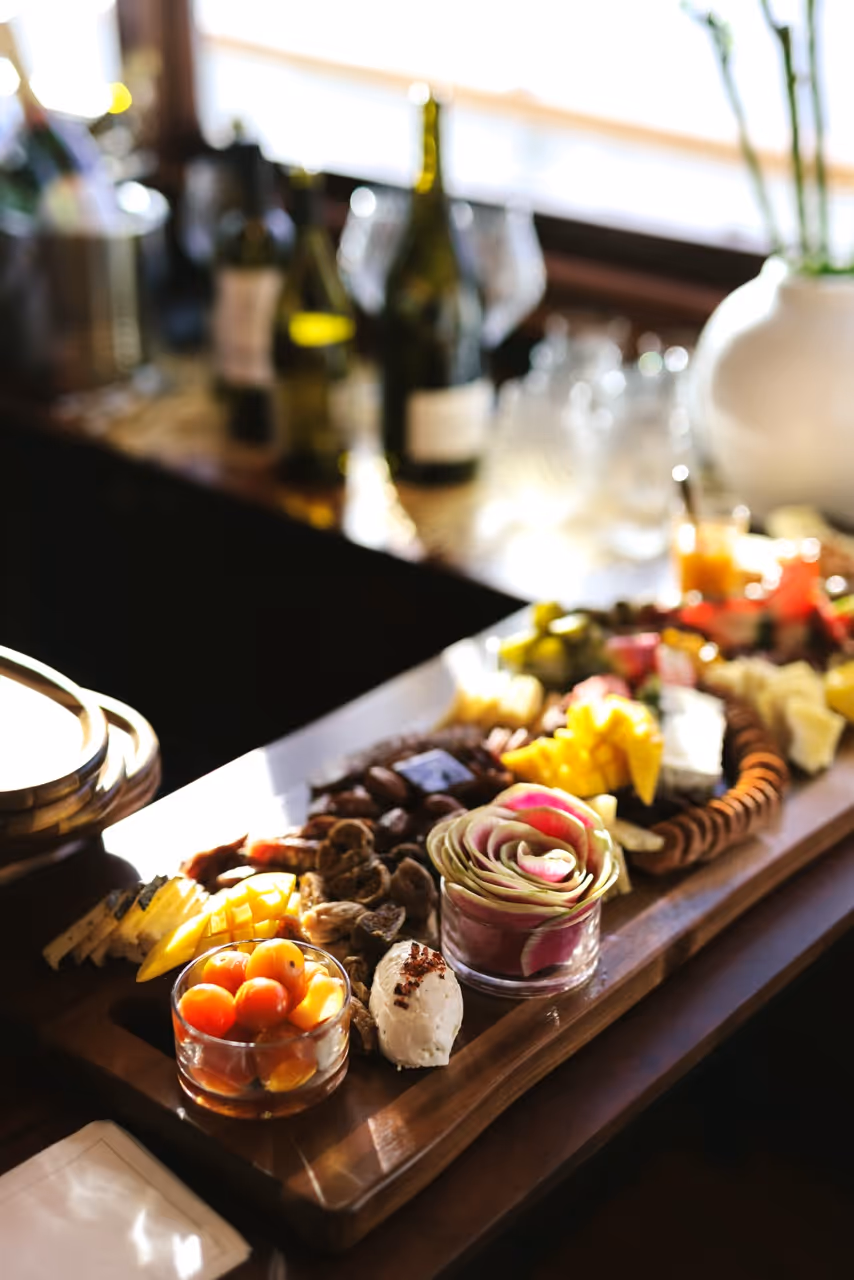 Gourmet charcuterie board with assorted cheeses, nuts, fruits, and a decorative vegetable rose on a wooden table.