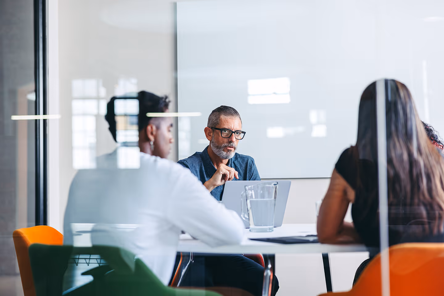Three people having a serious discussion in a modern office meeting room with a glass wall.