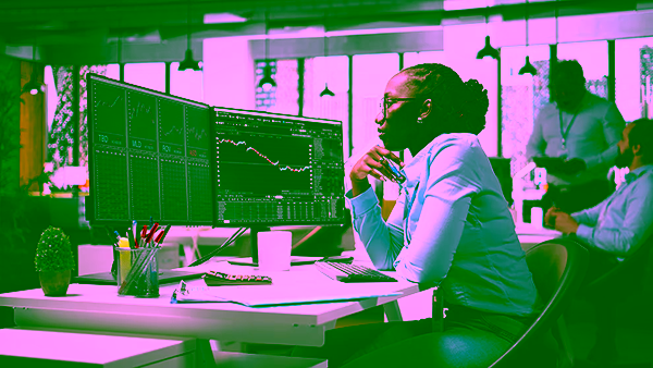 Businesswoman analyzing financial charts on dual computer monitors in modern office.