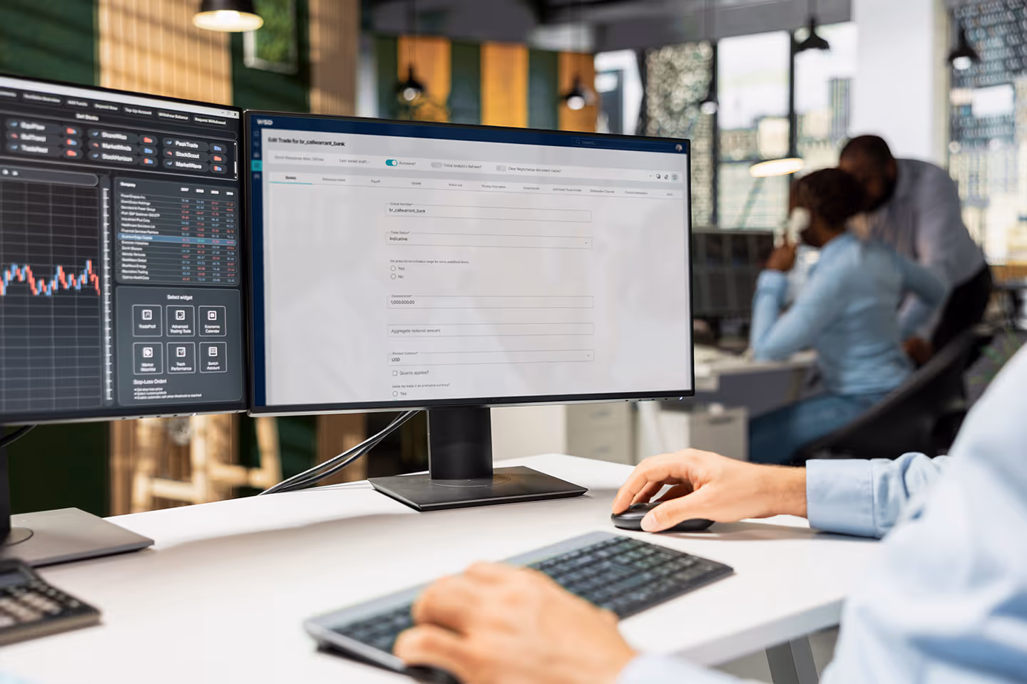 Close-up of person using a dual-monitor computer setup with financial data and trade editing software on screens in an office environment.