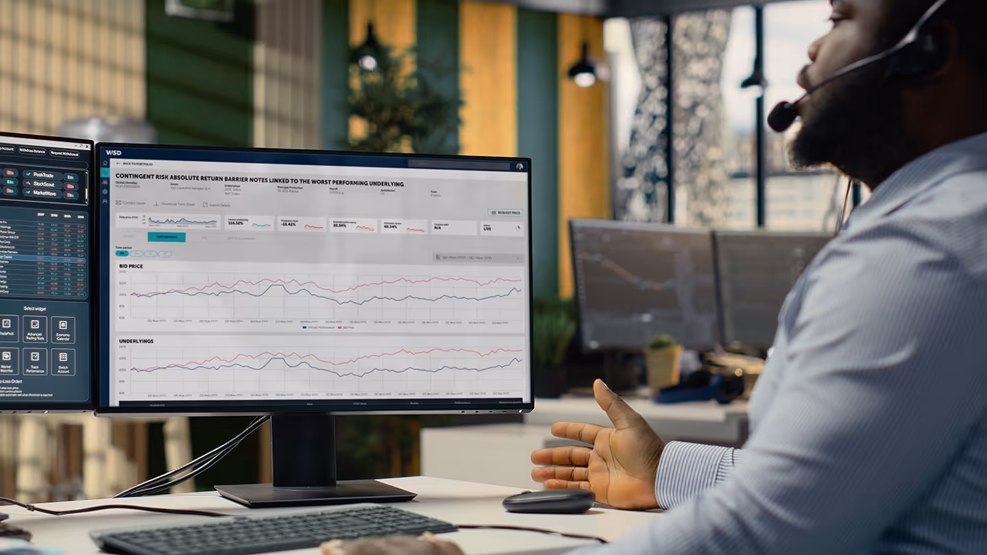 Man wearing headset analyzing financial graphs and data on dual computer monitors in a modern office.
