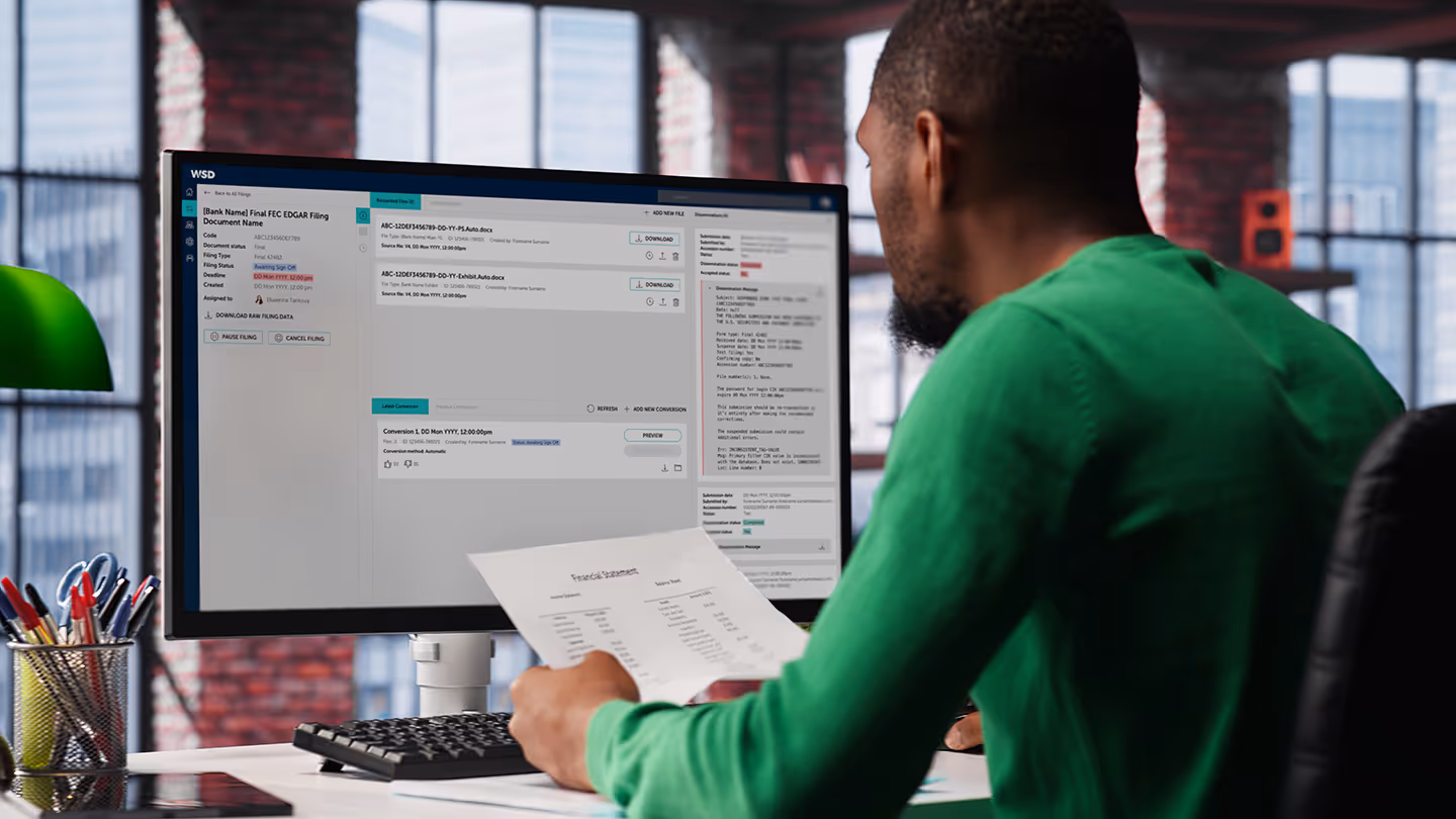 Over-the-shoulder view of a man in an office looking at financial data on a computer screen.