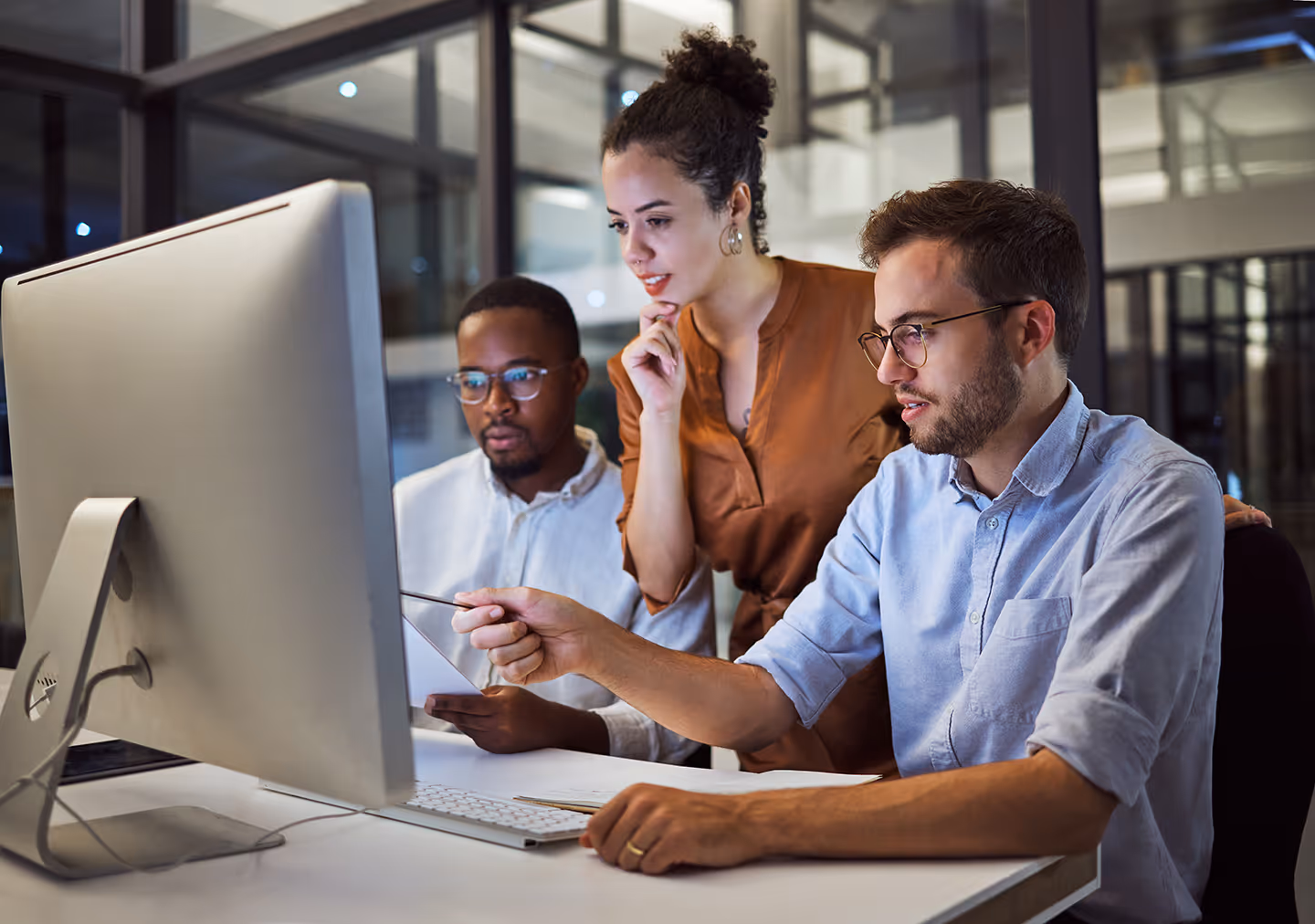 Three diverse colleagues collaborate on a project while looking at a large computer screen in a modern office.