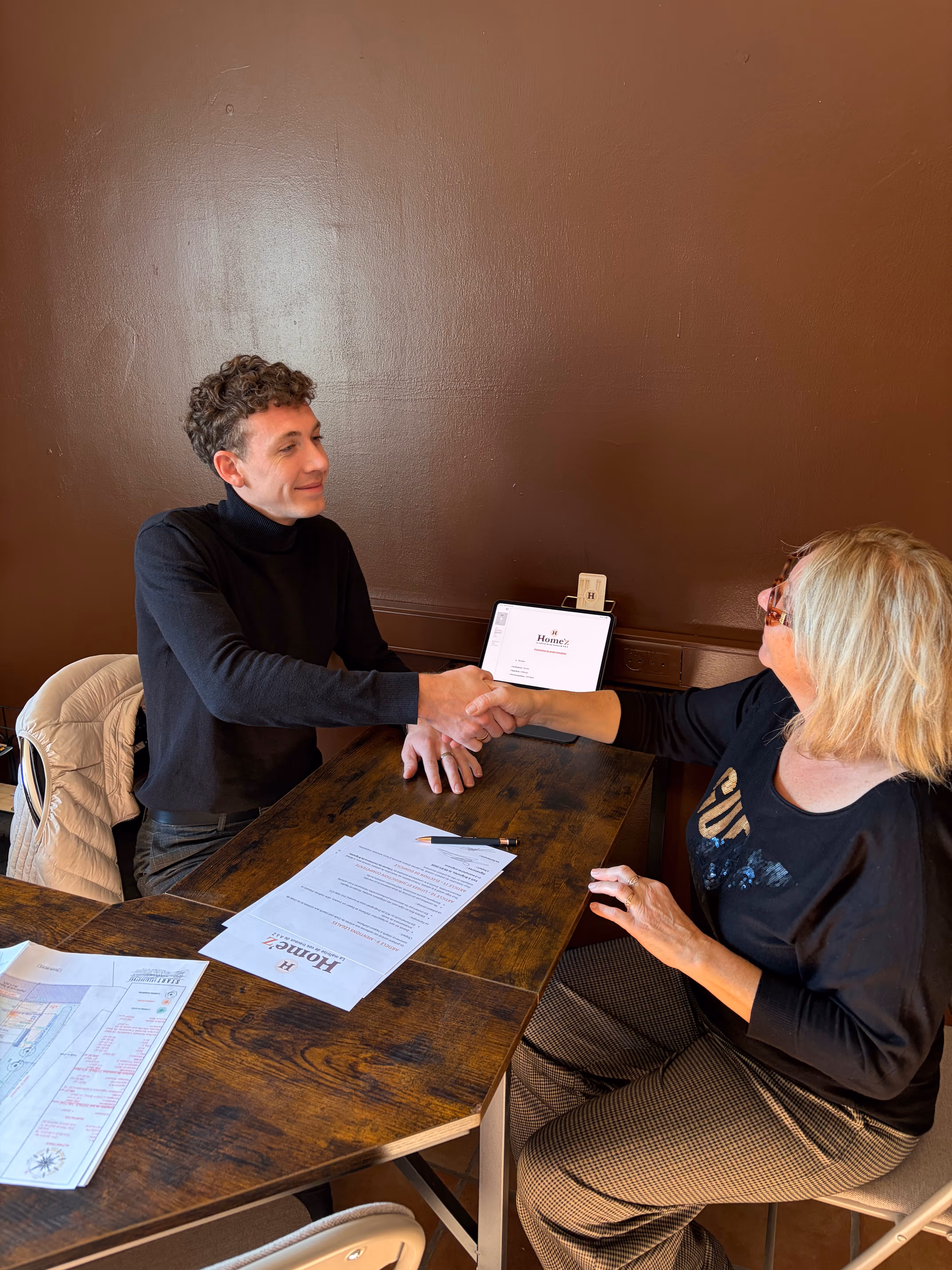 Un couple souriant et joyeux assis ensemble sur un canapé beige avec des coussins derrière eux.