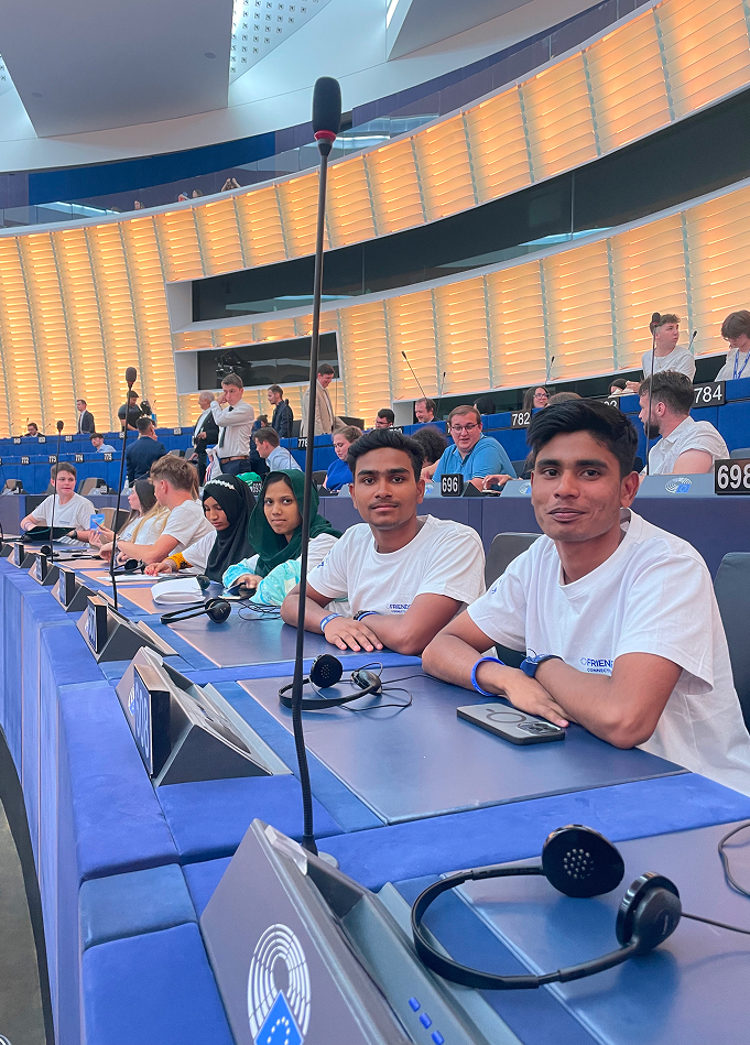 A diverse group of young people sitting at a conference table with headsets and microphones in a modern, curved auditorium.