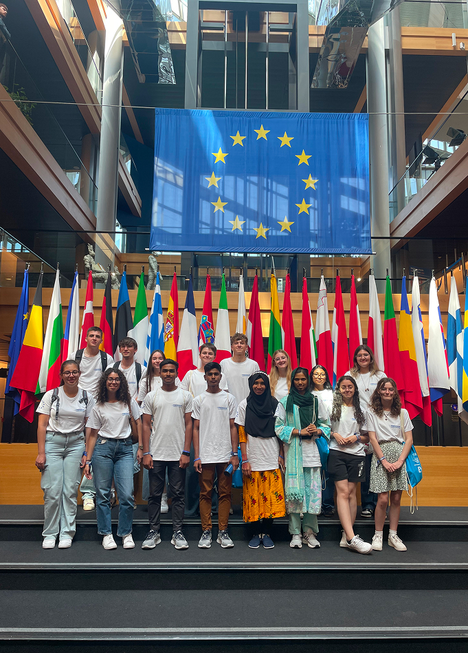 Group of diverse young people posing in front of European Union and member country flags inside a modern building.